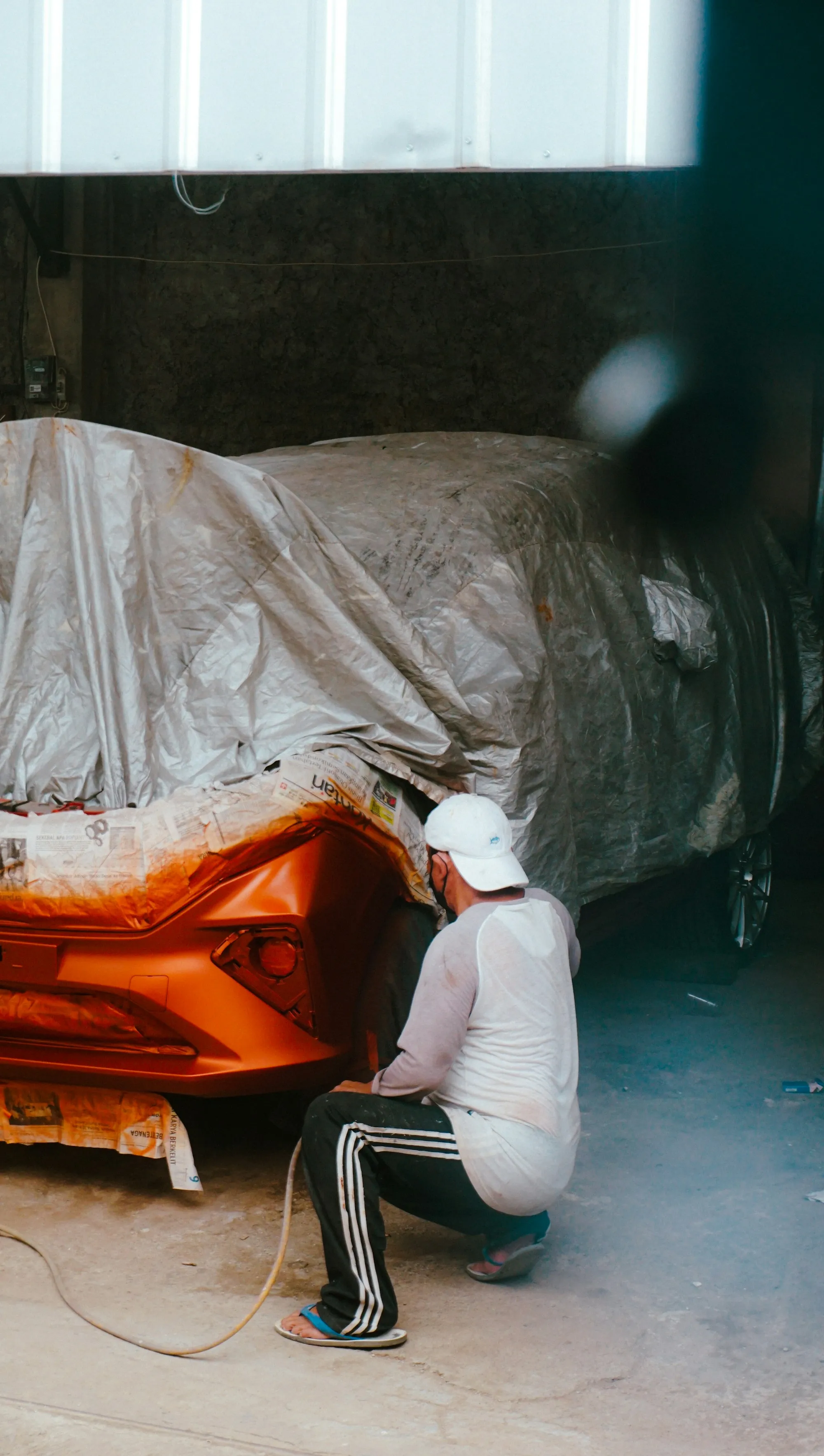 Painter in coveralls working on a car under protective plastic sheeting